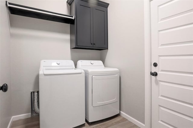 laundry area featuring cabinet space, baseboards, light wood-type flooring, and washing machine and dryer