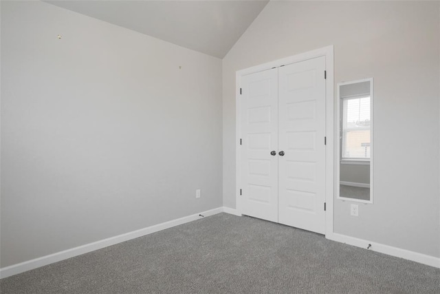 unfurnished bedroom with a closet, baseboards, dark colored carpet, and vaulted ceiling