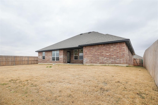 rear view of house with a shingled roof, a fenced backyard, a yard, and brick siding