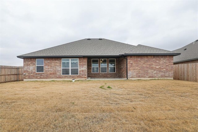 rear view of property with brick siding, a lawn, fence private yard, and roof with shingles