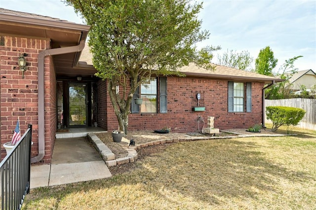 1113 Bank Side Cir, Edmond, OK 73012 - view of exterior entry featuring a lawn, brick siding, fence, and roof with shingles