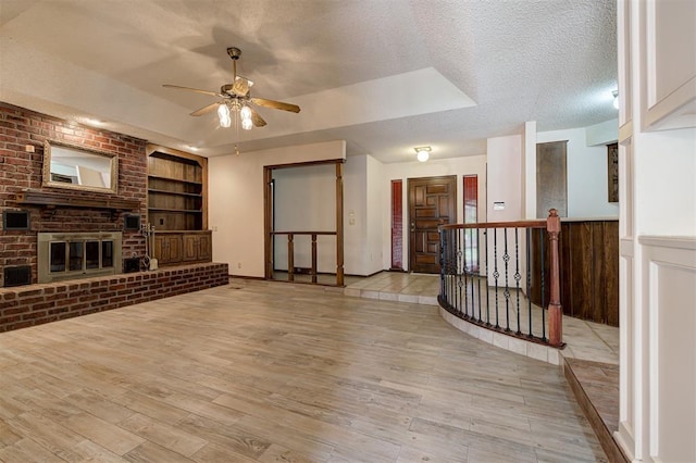 1113 Bank Side Cir, Edmond, OK 73012 - unfurnished living room with a textured ceiling, light wood-style floors, built in shelves, ceiling fan, and a tray ceiling