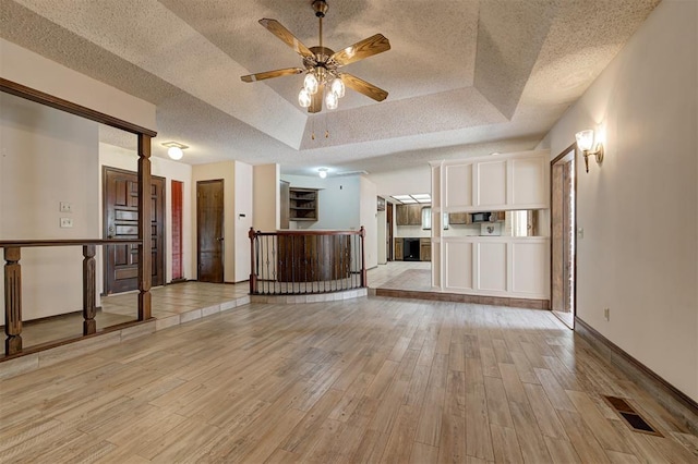1113 Bank Side Cir, Edmond, OK 73012 - unfurnished living room featuring a tray ceiling, a textured ceiling, visible vents, and light wood-style floors
