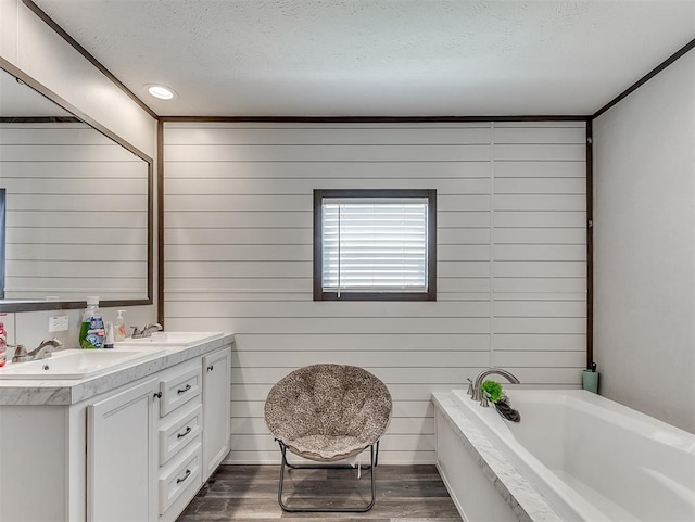 28737 Oakwood Meadows Dr, Cashion, OK 73016 - bathroom with a bathing tub, a sink, a textured ceiling, double vanity, and wood finished floors