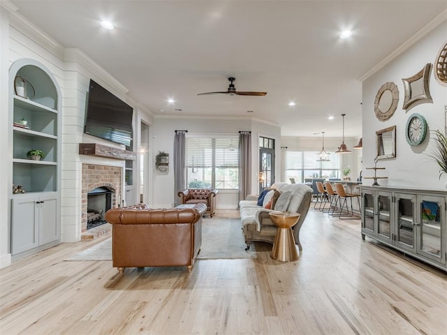 living area featuring light wood-type flooring, ornamental molding, a brick fireplace, and a ceiling fan