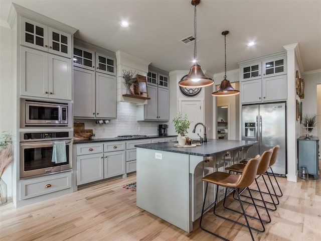 kitchen with appliances with stainless steel finishes, a sink, tasteful backsplash, visible vents, and a kitchen bar