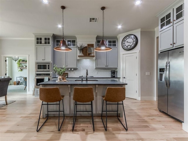 kitchen featuring an island with sink, stainless steel appliances, tasteful backsplash, visible vents, and ornamental molding