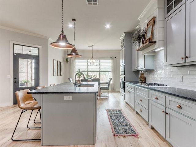 kitchen with a sink, appliances with stainless steel finishes, ornamental molding, and a kitchen island with sink