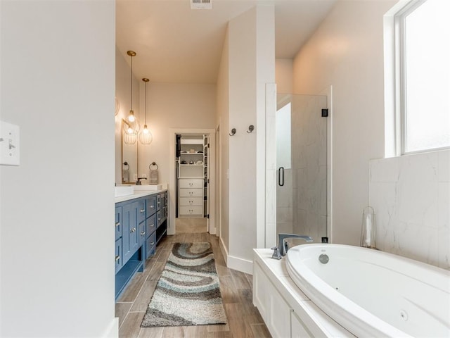 bathroom with vanity, wood finished floors, a jetted tub, a spacious closet, and a shower stall