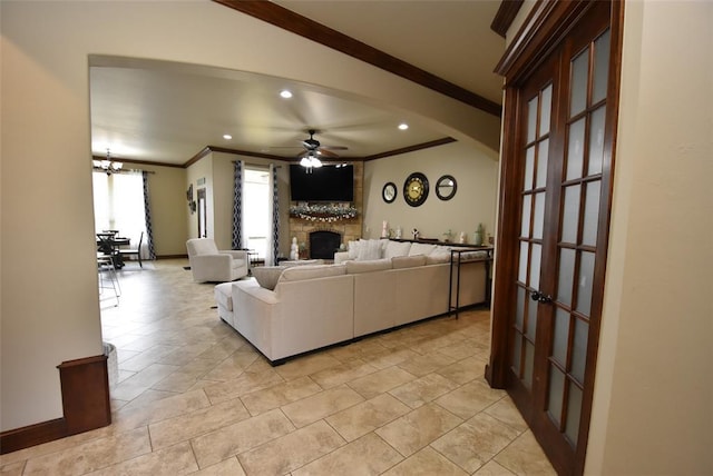 living room with arched walkways, ornamental molding, a stone fireplace, recessed lighting, and ceiling fan with notable chandelier