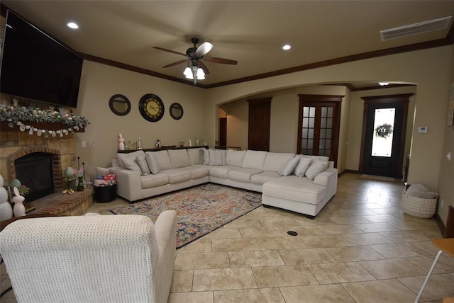 living room featuring visible vents, arched walkways, ornamental molding, ceiling fan, and a fireplace