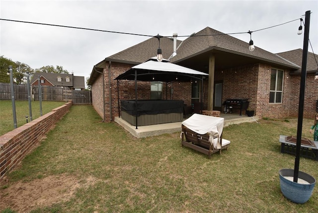 rear view of property featuring a hot tub, a yard, a fenced backyard, a patio area, and brick siding