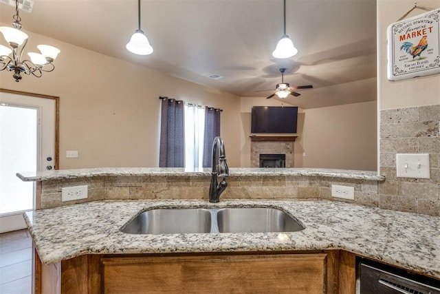 3719 Black Forrest Ct, Newcastle, OK 73065 - kitchen featuring ceiling fan with notable chandelier, a fireplace, light stone counters, a sink, and brown cabinets