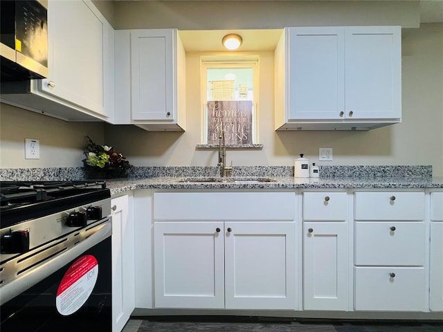 kitchen with gas range, white cabinetry, a sink, and light stone counters