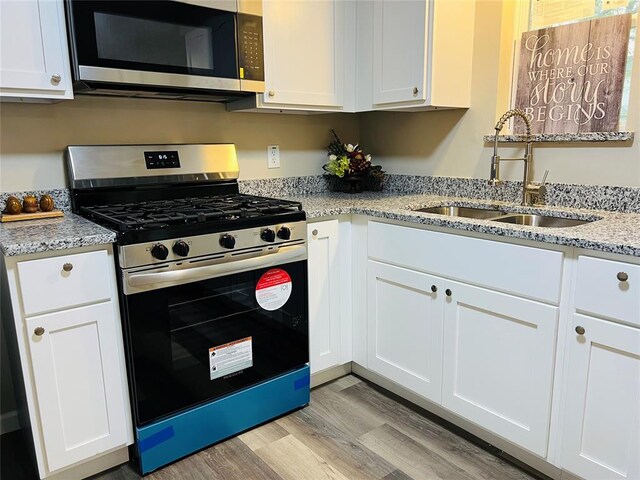 kitchen with light wood-style flooring, white cabinets, light stone countertops, appliances with stainless steel finishes, and a sink