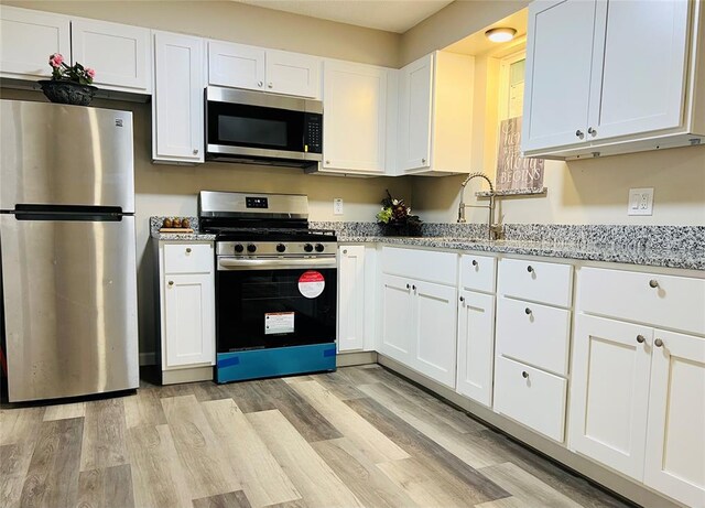 kitchen featuring white cabinets, a sink, appliances with stainless steel finishes, light wood-style floors, and light stone counters