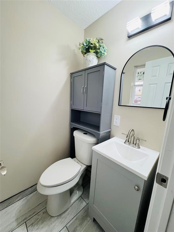 half bath with vanity, a textured ceiling, and toilet