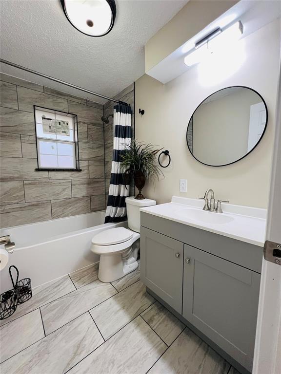 full bath with toilet, a textured ceiling, vanity, and shower / bath combo