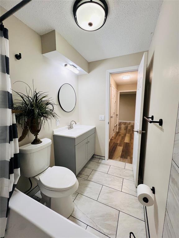 full bathroom featuring toilet, marble finish floor, vanity, and a textured ceiling