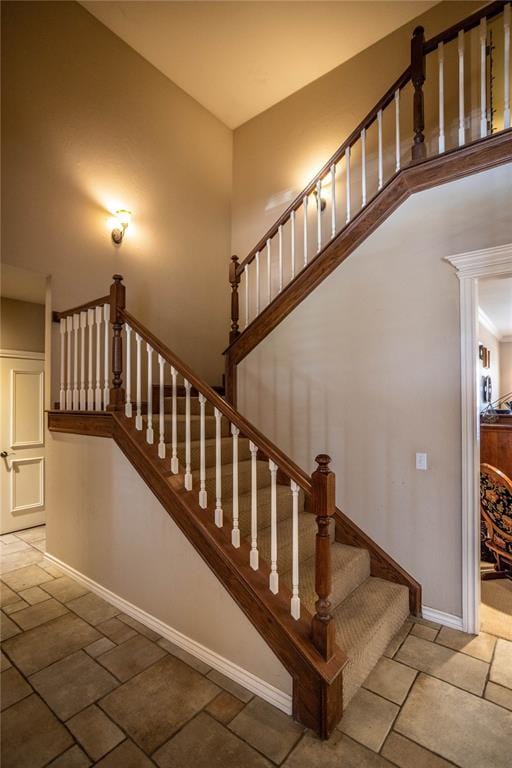 stairs with stone tile floors, a towering ceiling, and baseboards