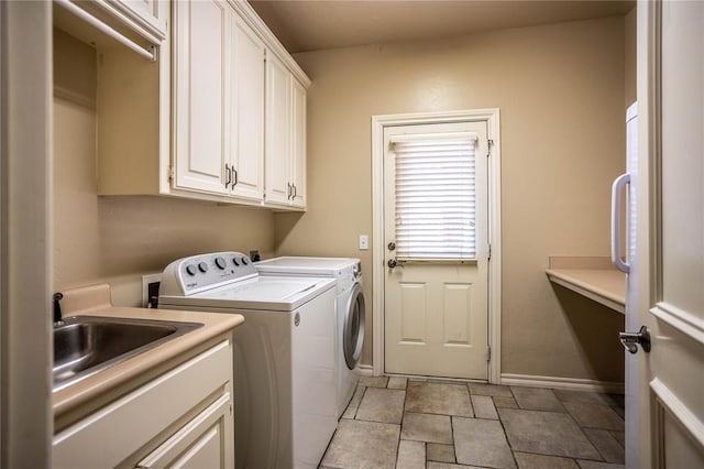 washroom featuring washer and clothes dryer, a sink, cabinet space, stone finish flooring, and baseboards