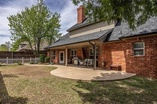 rear view of house with fence, roof with shingles, a patio area, a lawn, and brick siding