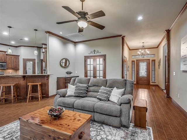 living room with visible vents, ornamental molding, wood finished floors, baseboards, and ceiling fan with notable chandelier