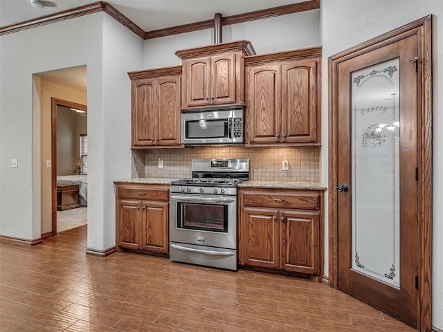 kitchen with crown molding, brown cabinetry, backsplash, and stainless steel appliances