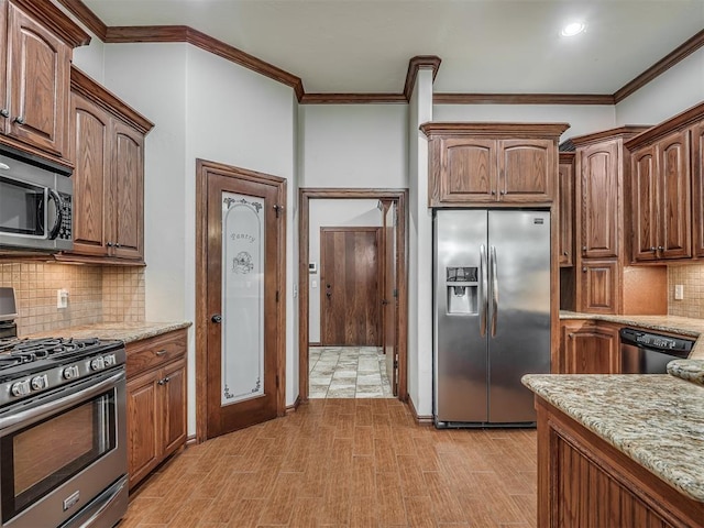 kitchen featuring backsplash, light stone counters, light wood-style floors, ornamental molding, and stainless steel appliances