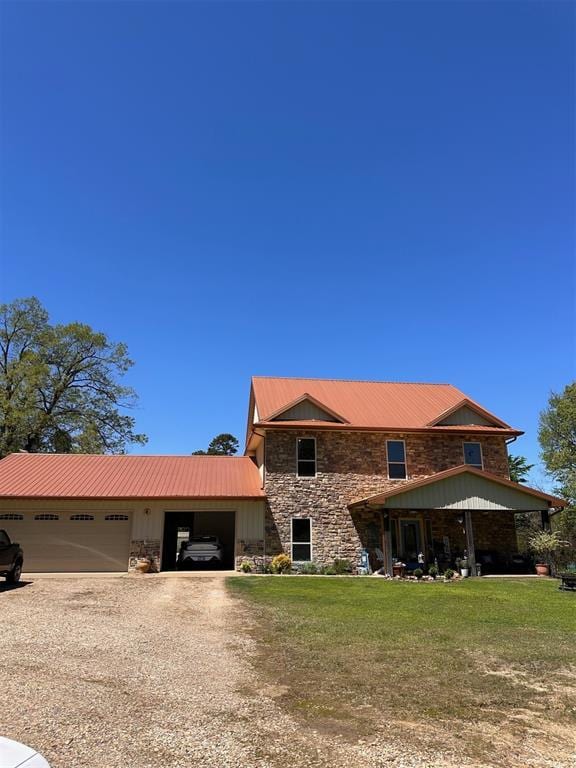 traditional home with driveway, stone siding, a front yard, a garage, and metal roof