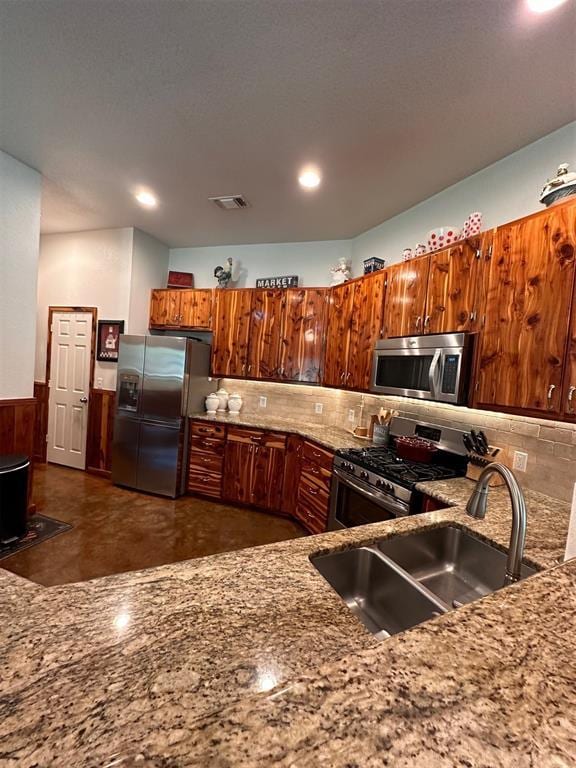 kitchen featuring tasteful backsplash, a sink, brown cabinets, light stone countertops, and stainless steel appliances