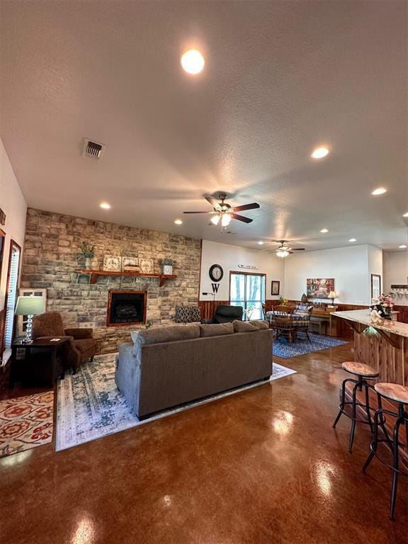 living area featuring a stone fireplace, recessed lighting, a ceiling fan, visible vents, and concrete flooring