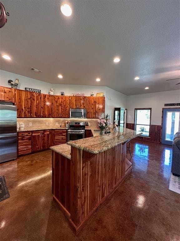 kitchen with brown cabinets, recessed lighting, a breakfast bar, light stone countertops, and appliances with stainless steel finishes