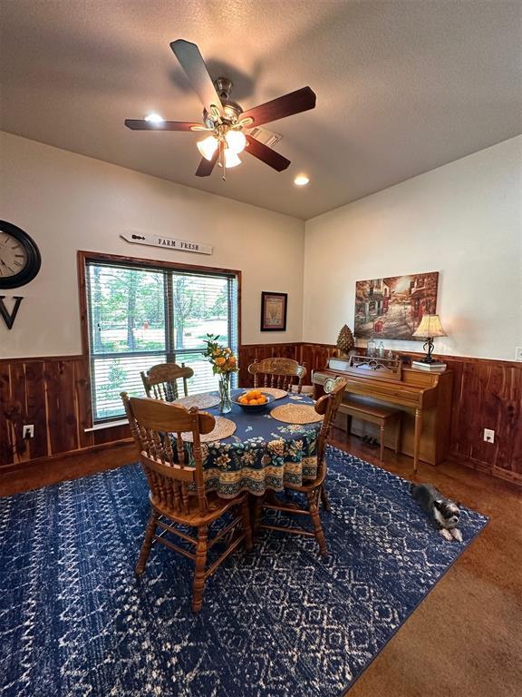 dining area with wooden walls, a textured ceiling, carpet floors, wainscoting, and ceiling fan