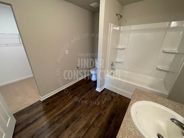 full bathroom with shower / bathing tub combination, toilet, wood finished floors, a sink, and baseboards