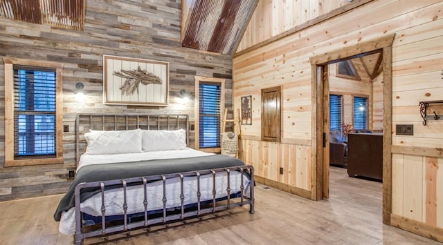 bedroom featuring light wood-type flooring, high vaulted ceiling, and wood walls