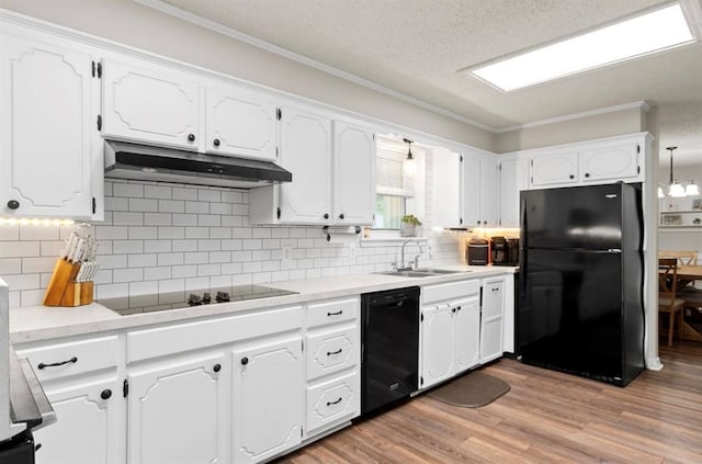 kitchen with a sink, white cabinetry, black appliances, under cabinet range hood, and ornamental molding