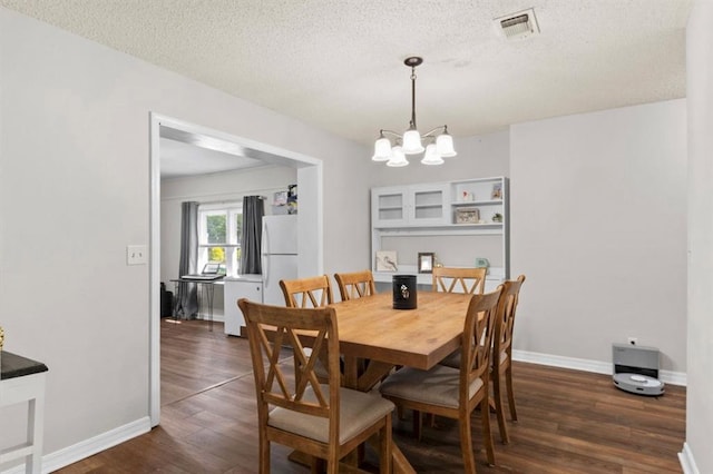 dining room with a textured ceiling, dark wood-style flooring, baseboards, visible vents, and a chandelier