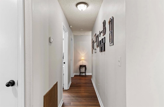 hallway with wood finished floors, a textured ceiling, baseboards, and visible vents
