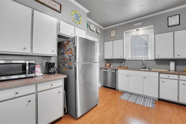 121 S Randlett St, Hobart, OK 73651 - kitchen with ornamental molding, a textured ceiling, white cabinetry, light wood-style floors, and stainless steel appliances