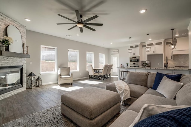 living room with baseboards, ceiling fan, a fireplace, recessed lighting, and dark wood-type flooring