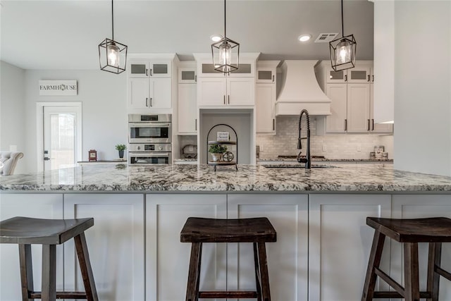 kitchen with stainless steel double oven, white cabinetry, visible vents, a sink, and decorative backsplash