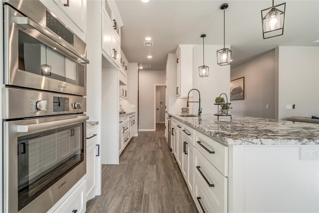 kitchen featuring wood finished floors, stainless steel double oven, a sink, and white cabinetry