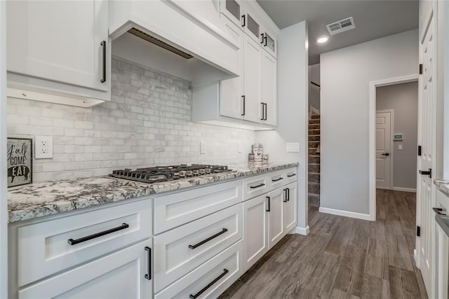 kitchen with glass insert cabinets, visible vents, stainless steel gas cooktop, and light stone counters