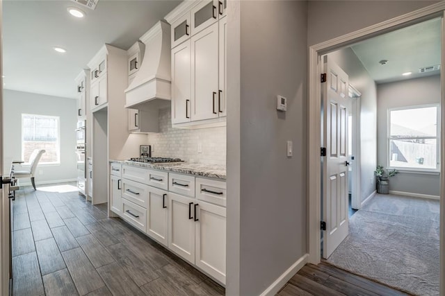 kitchen featuring custom exhaust hood, baseboards, glass insert cabinets, backsplash, and stainless steel gas cooktop