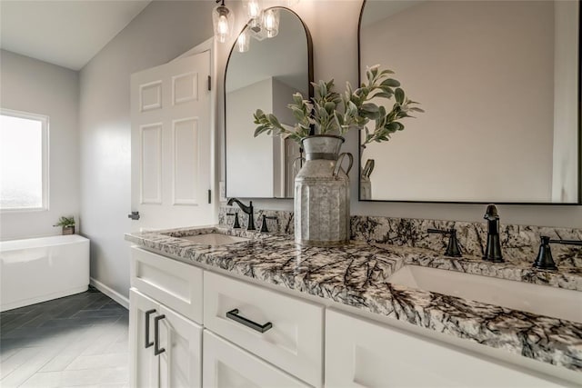 bathroom with a soaking tub, double vanity, a sink, and baseboards
