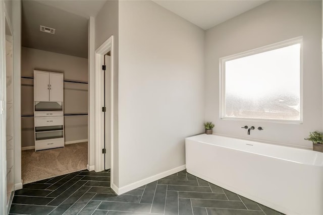 bathroom featuring a freestanding bath, baseboards, tile patterned flooring, and visible vents