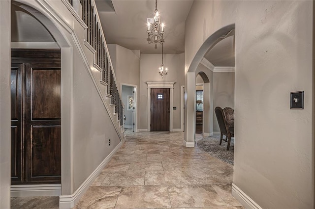 foyer entrance featuring a chandelier, arched walkways, baseboards, and stairs