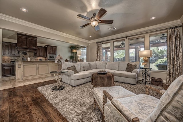 living area with visible vents, baseboards, ornamental molding, a ceiling fan, and light wood-style flooring