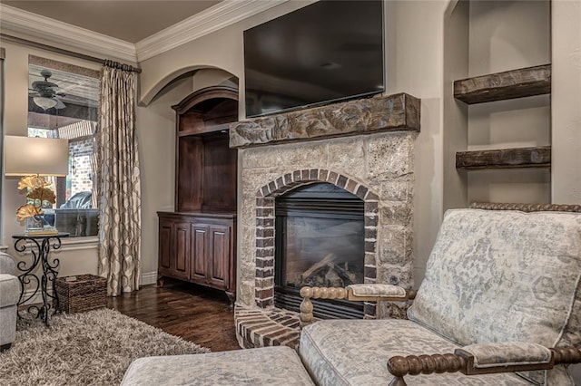 living area featuring baseboards, a fireplace, dark wood finished floors, crown molding, and ceiling fan